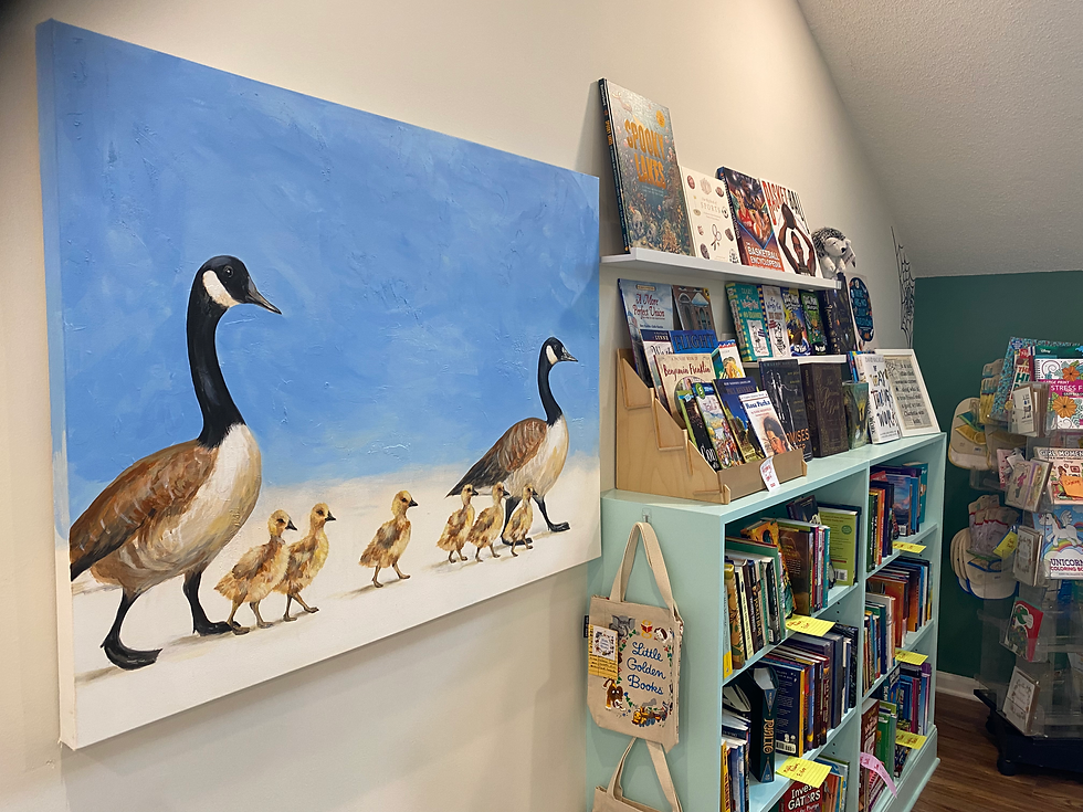 Painted geese with goslings on a blue wall beside a mint bookcase filled with children’s books in a cozy reading nook