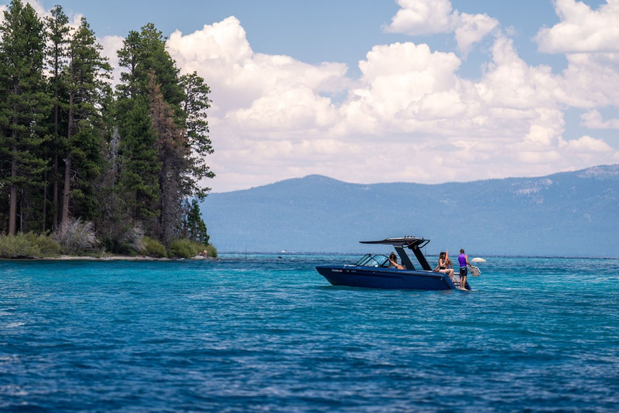 Navy wake boat anchored in turquoise water by a pine-covered point. Photograph by Jordan Orsak