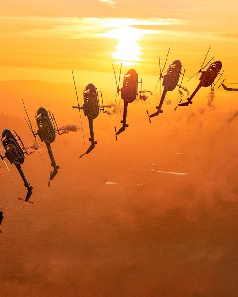 A formation of helicopters flying inverted at sunset