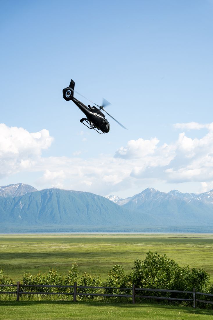 A helicopter flying over green Alaskan fields