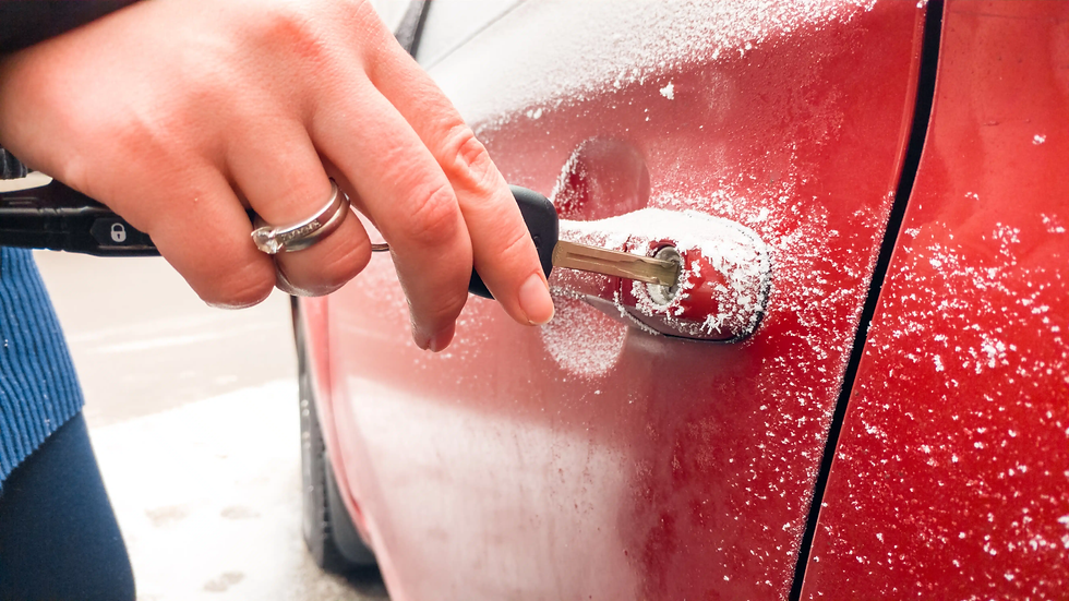 Hand with rings unlocking a red car door covered in frost with a key, set in a cold outdoor environment, creating a chilly mood.