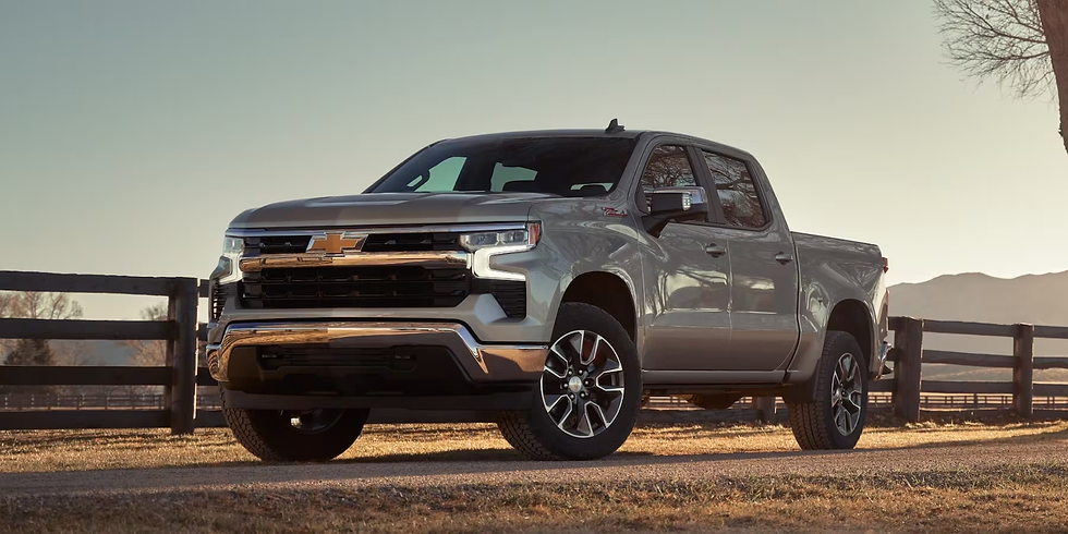 Silver pickup truck on dirt road, foreground. Wooden fence and leafless trees in the background. Mountain range under a clear sky. Calm mood.
