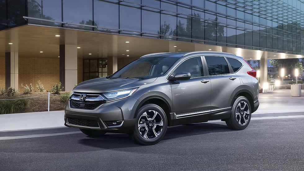 Gray SUV parked outside a modern glass building. Evening lights illuminate the scene, reflecting on the car's metallic surface. Quiet and sleek mood.
