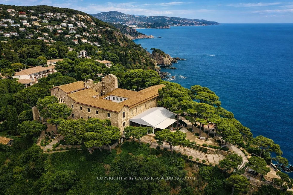 Oceanfront villa wedding on the Costa Brava, styled and coordinated by Casamiga Weddings, in Convent de Blanes Stone seaside terrace beside rustic building with lanterns, potted plants and pine trees; watermark Casamiga-weddings.com.