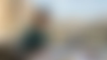 Продление DNV Испания документы digital nomad visa Spain renewal юристы Atanesov Petrova. Женщина пишет за столом на террасе с видом на город. На столе ноутбук, документы, табличка с текстом. На заднем плане видна архитектура.