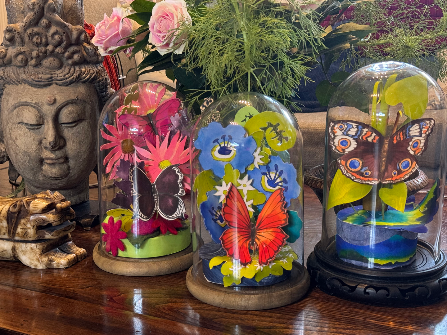 Three Separate Butterfly paper dimensional sculptures under glass domes, each with flowers and leaves with butterflies perched upon.