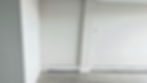 Empty office room with light gray walls and wood flooring. A baseboard heater is visible along the wall. The mood is minimalistic and clean.