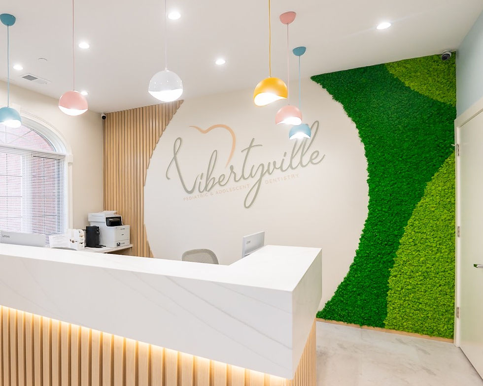 Dental clinic reception with curved green reindeer moss wall, marble counter, wood slats, and pastel pendant lights
