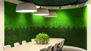 Curved meeting room with floor-to-ceiling green reindeer moss wall, wooden conference table, and modern pendant lights