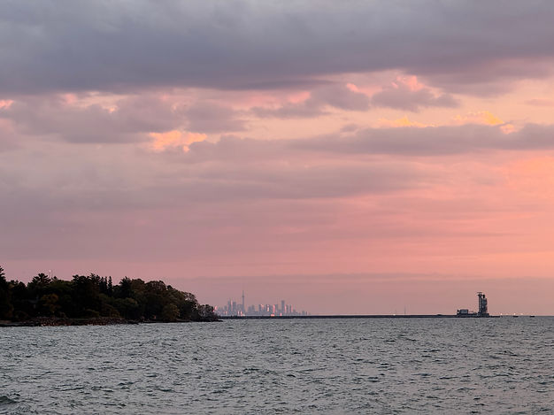 Soft pink sunset over Lake Ontario shoreline with distant lighthouse silhouette