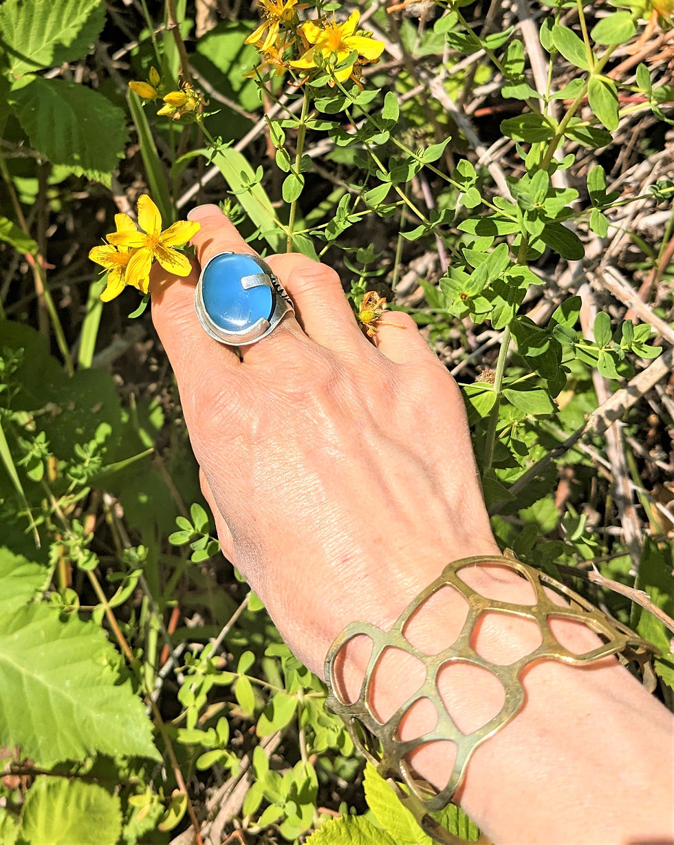 Woman picking St. John's Wort yellow flowers on sunny day in wild. Wearing blue and silver ring by BM Charmed and brass cuff bracelet by Ambient Studios.