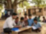 Outdoor photography. A teacher guides young students in assembling an electronic circuit board in a rural school setting.
