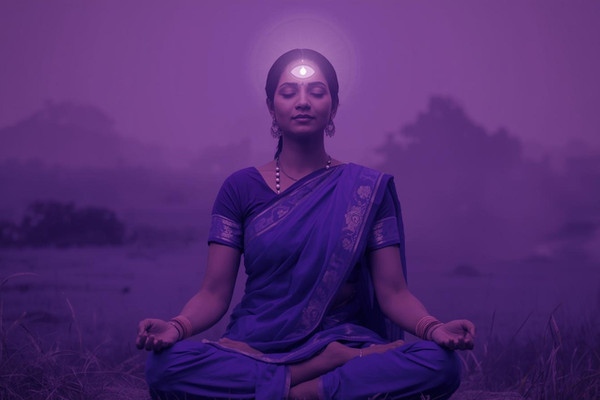 Realistic Indian woman in indigo saree meditating on third eye chakra with glowing Ajna energy in a serene natural background