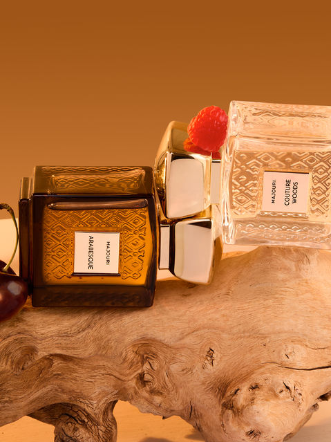 Parfums MAJOURI Arabesque et Couture Woods réunis sur un décor de bois et de sable, fond orangé