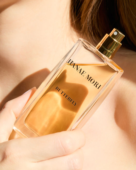 Main tenant un flacon de parfum Hanae Mori contre l'épaule, photographie parfum en lumière douce