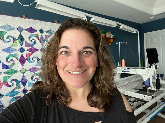 Photo of Michelle Russell standing in front of her longarm and a quilt on a design wall
