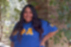 a girl with a blue shirt with greek letters Theta Phi Alpha standing in front of a brick wall
