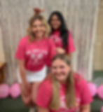 three women with salmon shirts stand in front of one another with their hand hovering over each other's heads in front of a silver backdrop