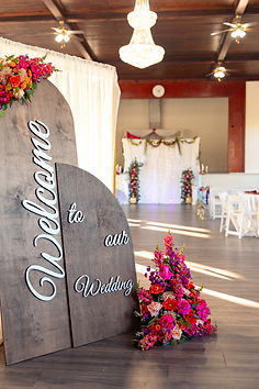 A sign that says welcome to our wedding decorated in brightly colored flowers