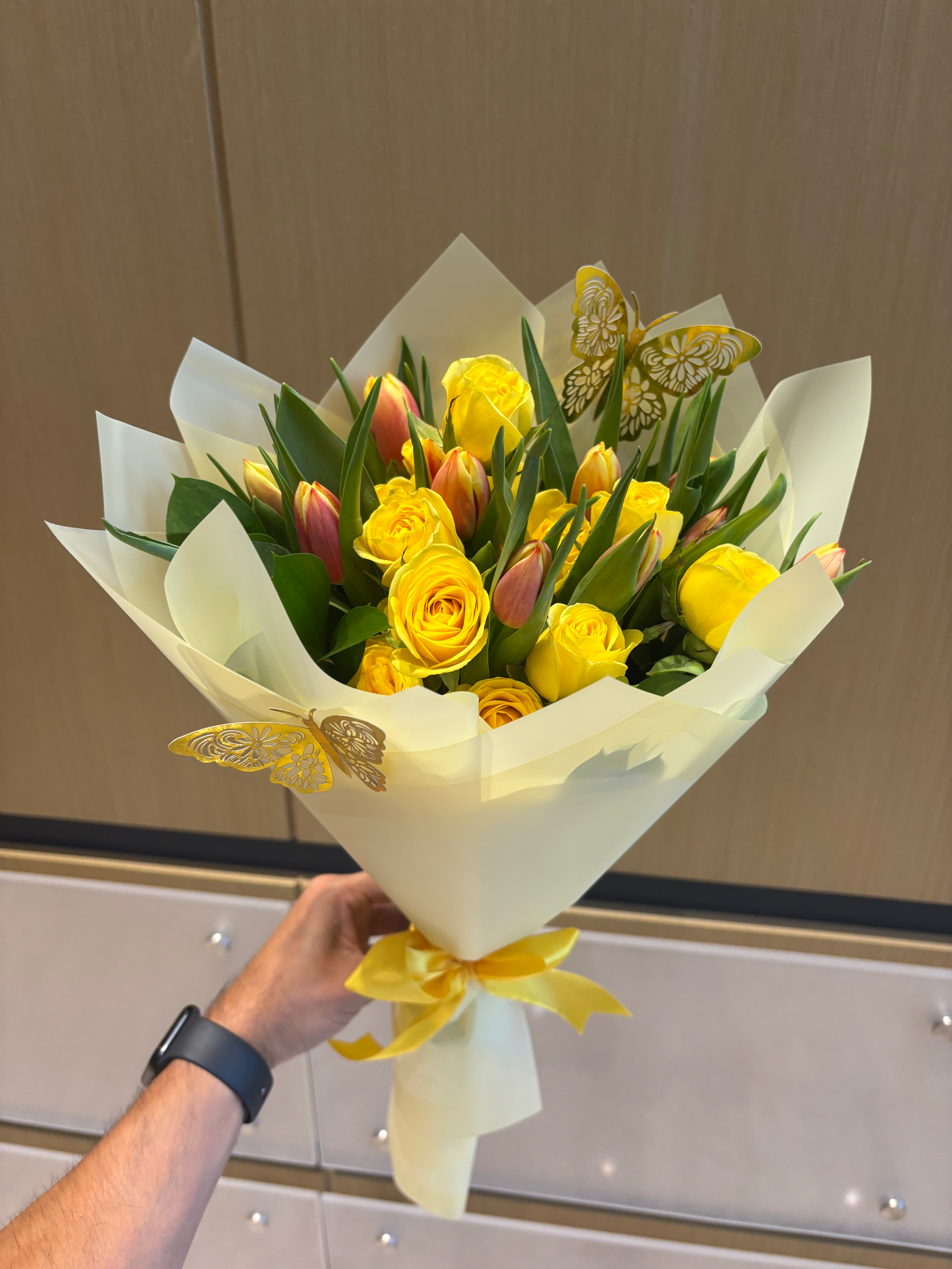 Vibrant bouquet of yellow roses and tulips, tied with a ribbon, decorated with butterflies.