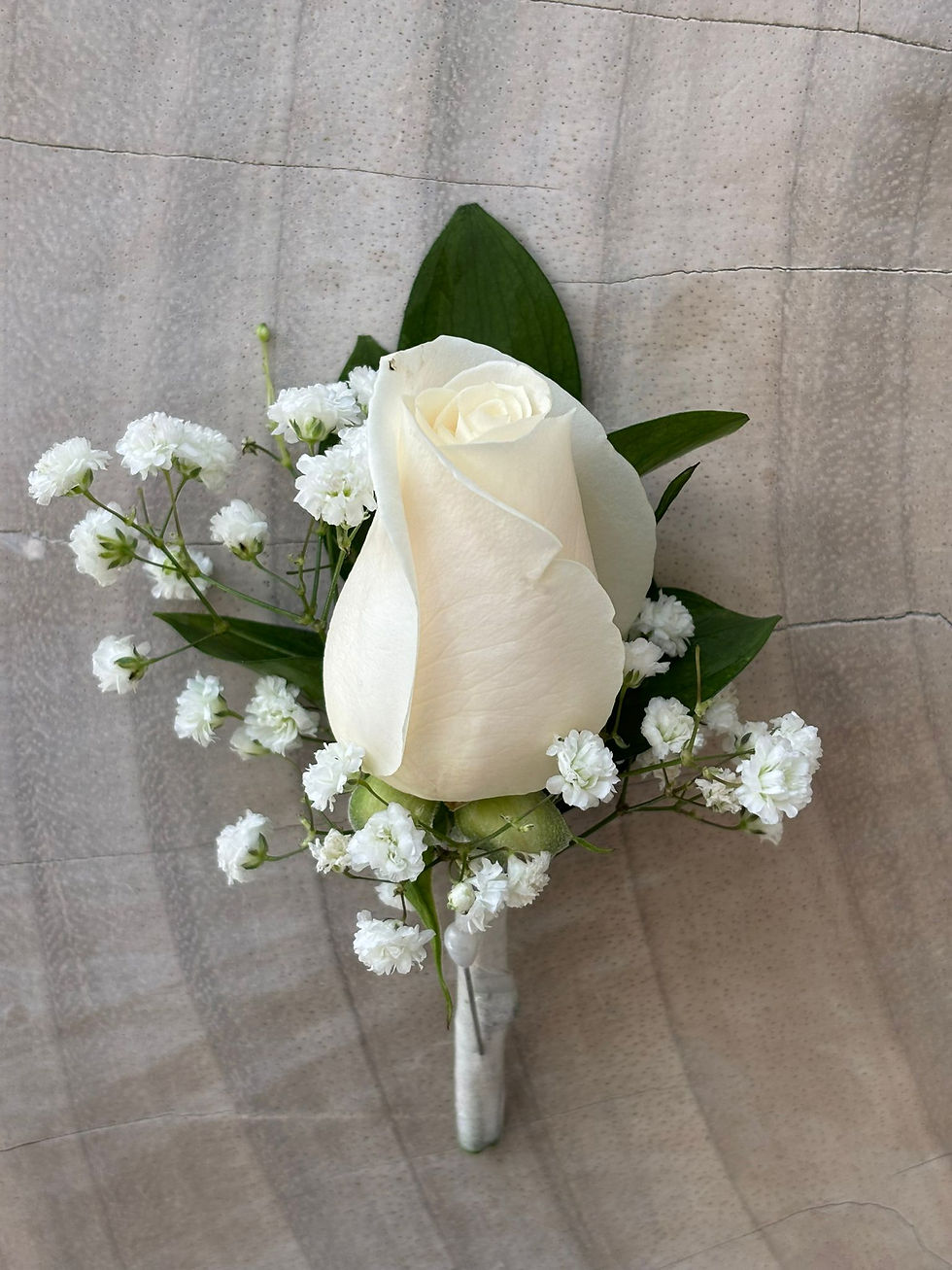 Close-up of a white rose with baby's breath and green leaves.