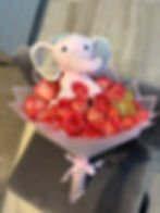 Pink stuffed elephant sitting on a bouquet of red roses. Doral Blooms