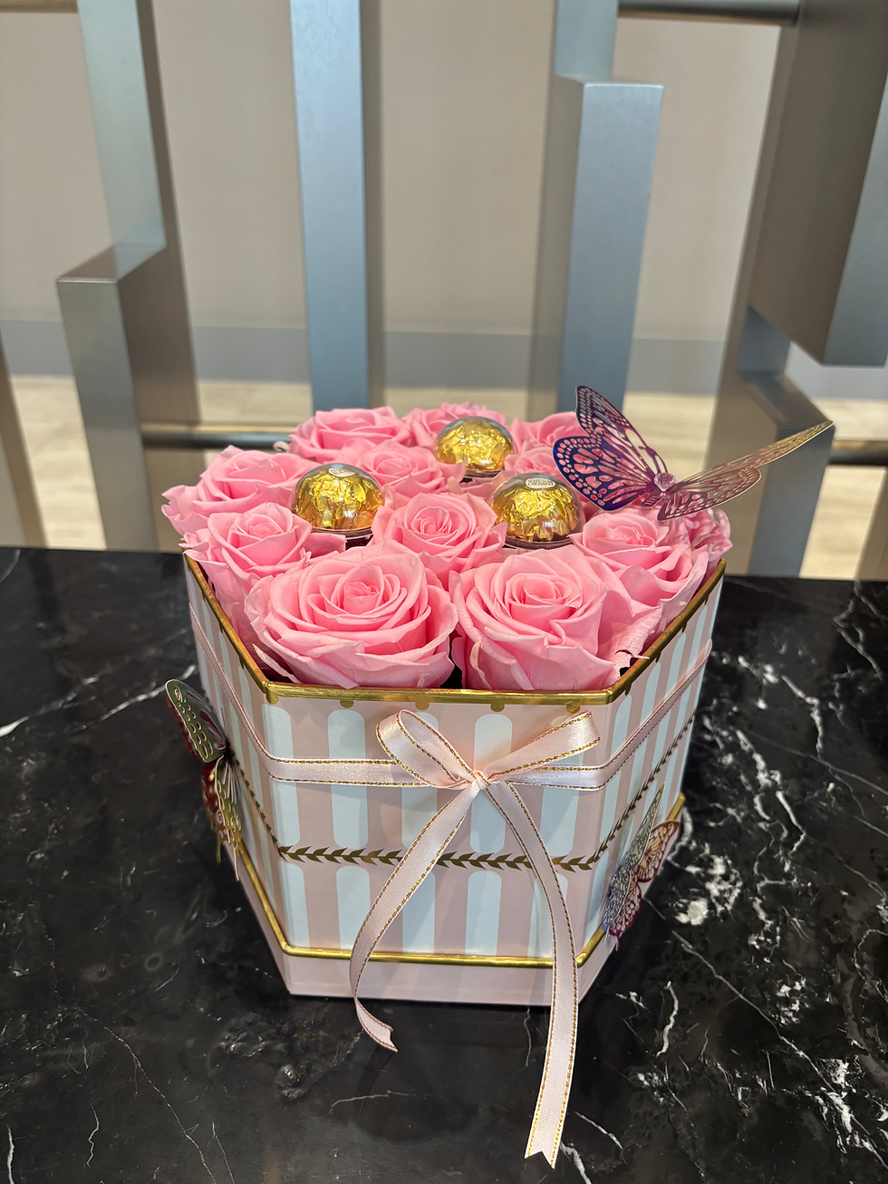Pink roses in a striped box with chocolates and ribbon.
