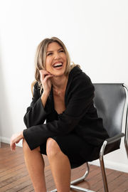 a woman in a black jacket is sitting in a chair and smiling