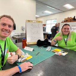 two team members sitting at their table giving thumbs up wearing lime green team shirts