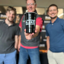 tom gray standing between two guys holding a black cup