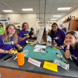stellar tech girls four team members sitting at their work table wearing purple team shirts