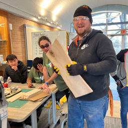 tool tech adam holding a piece of rectangle wood in the makerspace