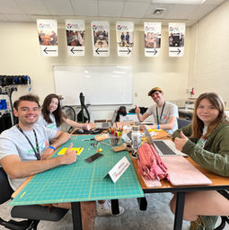 team of four sitting at their table giving thumbs up wearing grey team shirts