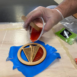 someone pouring orange epoxy into a wooden cut out airplane
