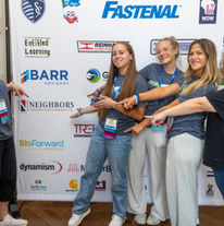 Team CTEC CAPS Creators pointing to their team sponsor logo Neighbors Construction on the step and repeat banner.