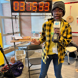 team member wearing yellow team shirt holding a news channel 41 microphone talking into it in front of the make48 48 hour clock
