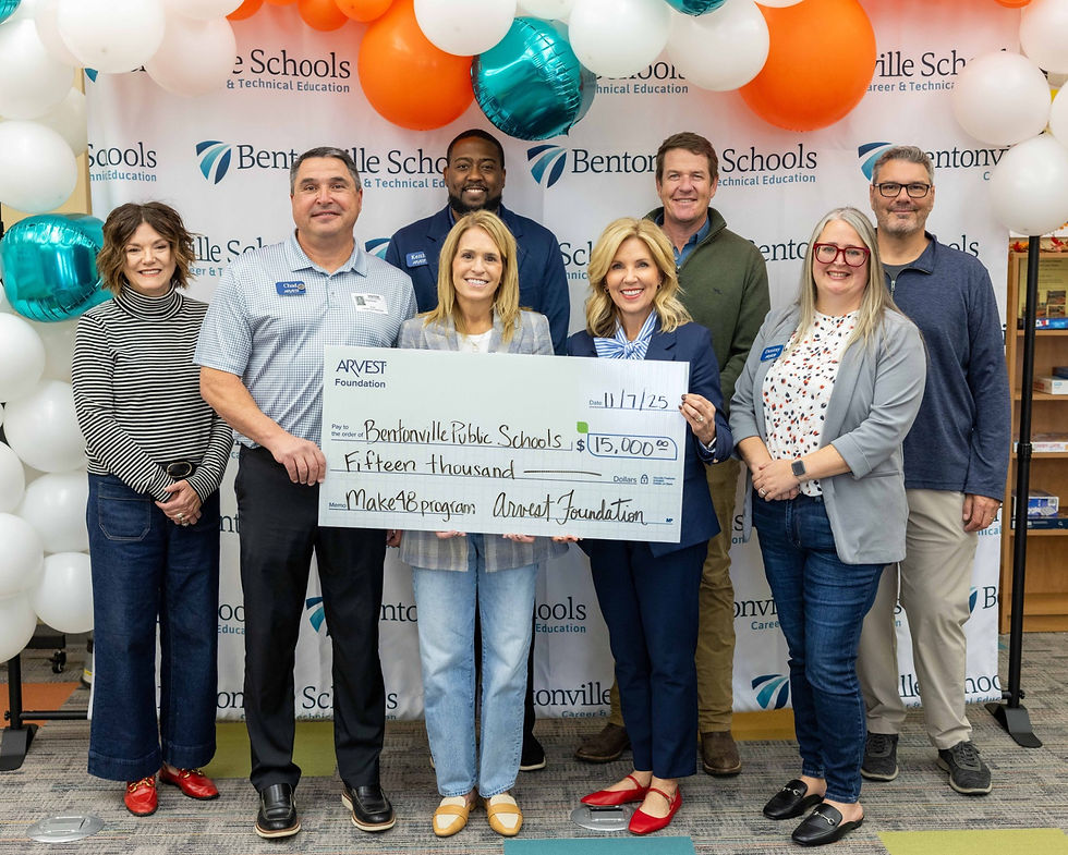 Several adults posing in front of Bentonville Schools banner and balloons holding large check