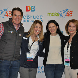 Group photo of Tom Gray, Leigh-Anne, Amy, and Ann standing in front of the debruce foundation step and repeat banner