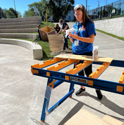 team member in blue team shirt working on her prototype outside standing by the gridlock table