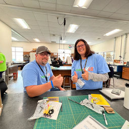 two team members giving thumbs up wearing light blue team shirts