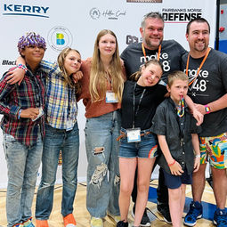 Tool techs and family members pose in front of a sponsor banner.