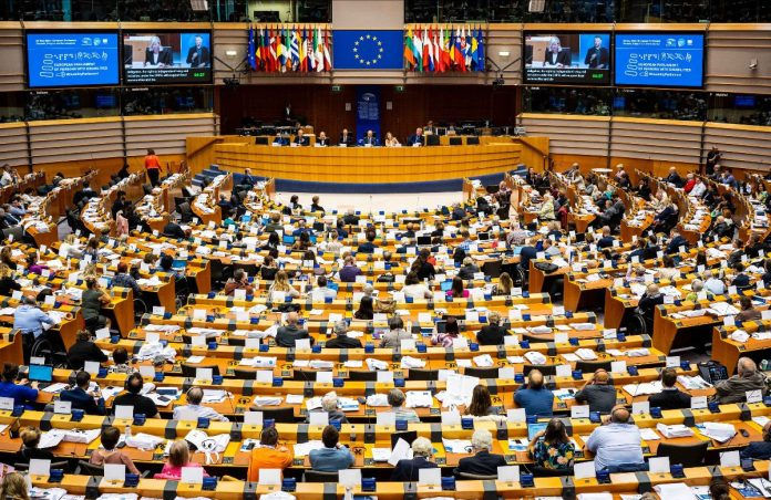 Mais de 600 pessoas reunem-se sentadas num auditório. Ao centro, atrás da mesa da presidência, está exposta a bandeira da União Europeia, ladeada pelas bandeiras hasteadas dos países membros.