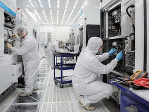 Technicians performing maintenance and diagnostics on Applied Materials semiconductor manufacturing equipment inside a cleanroom fabrication facility.