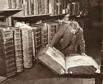 Vintage black and white photo of woman on the floor reading a giant book.