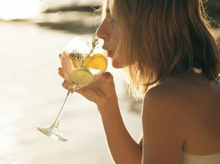 Woman drinking gin in a goblet glass in front of the ocean