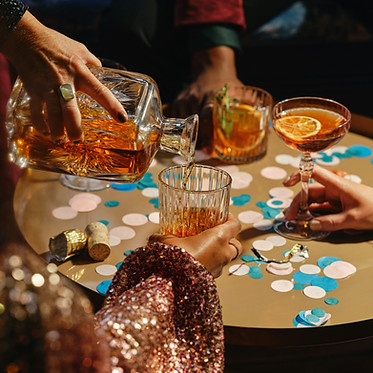 OurWhisky Foundation - Friends enjoying cocktails at a table with confetti