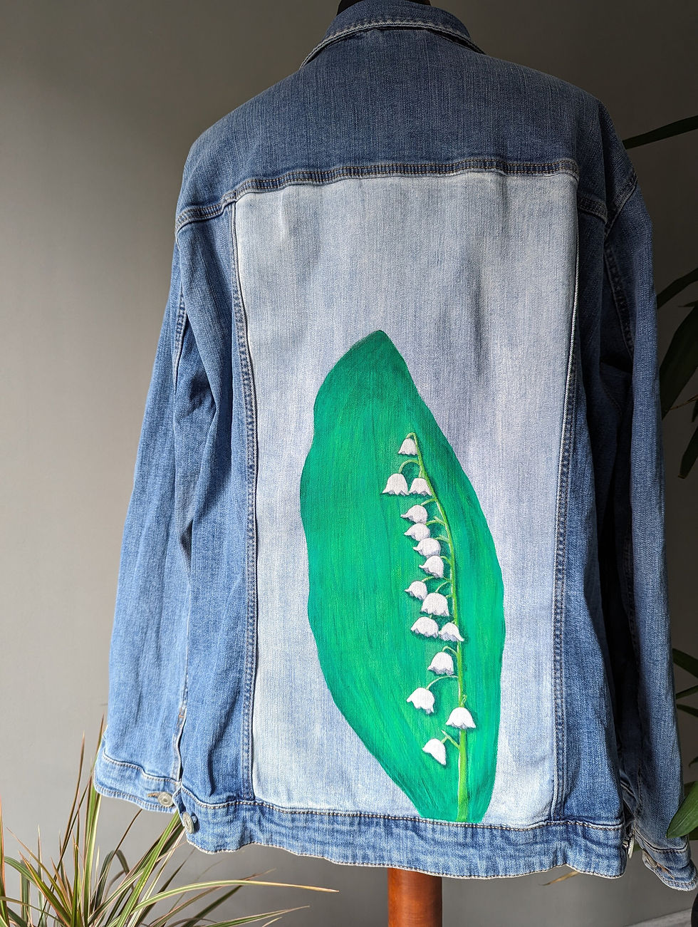 Miniaturbild: Hellblaue Jeansjacke, handbemalter Rücken. Hintergrund ist weiß, im Vordergrund ein Blatt und ein Zweig Maiglöckchen