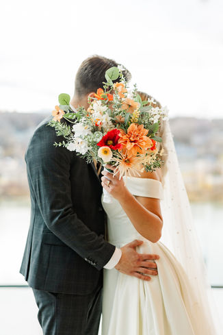 Bride and groom sharing kiss behind bouquet