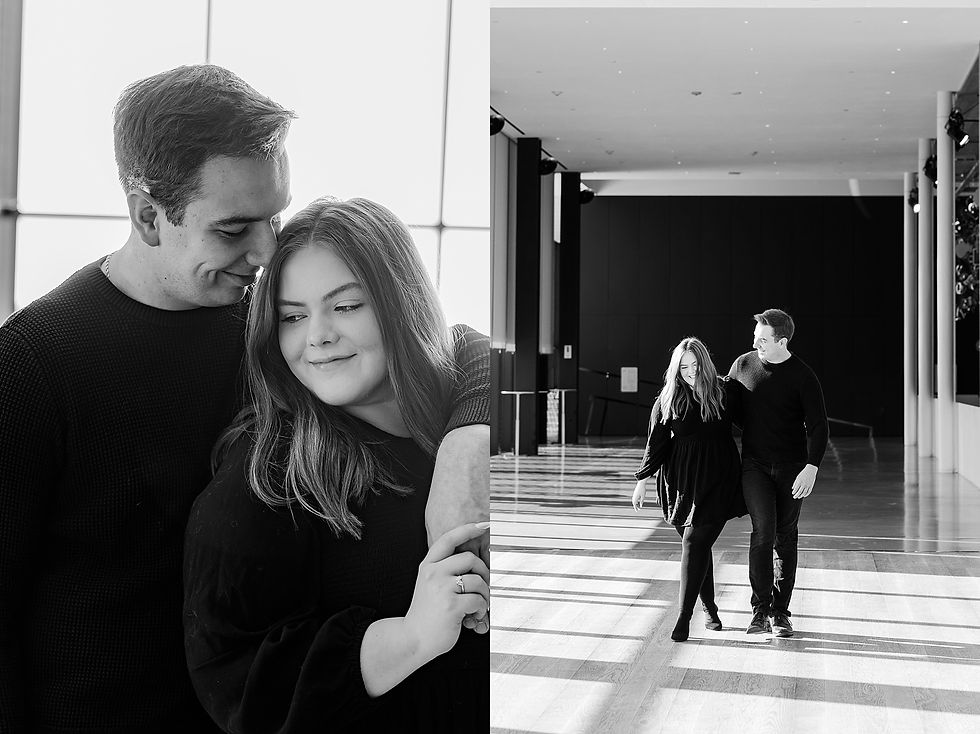 A couple in black outfits embrace and walk indoors with large windows; the mood is intimate and joyful. Black and white image.
