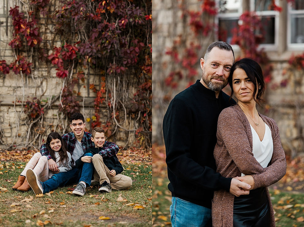 Family in park: three kids sit laughing on grass; couple stands embracing. Stone wall with red ivy in background. Autumn vibes.